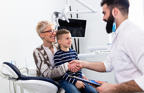 Young boy shaking hands with his dentist while sitting in his mothers lap