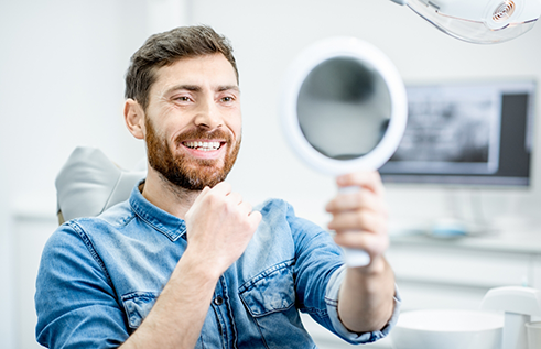 Man in dental chair looking at his smile in a mirror