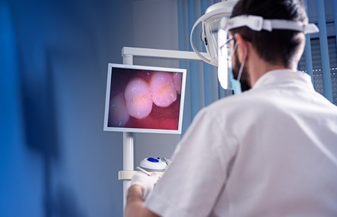 Dentist taking close up photos of a patients teeth and looking at them on a nearby monitor