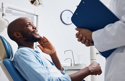 Man holding his cheek while talking to emergency dentist