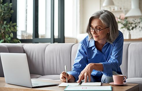 Woman filling out paperwork while looking at laptop