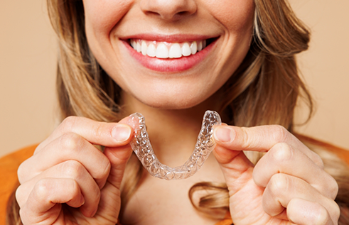 Smiling woman holding an Invisalign clear aligner